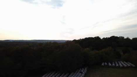 dolly left shot of a dense forest and wrapped hay bales