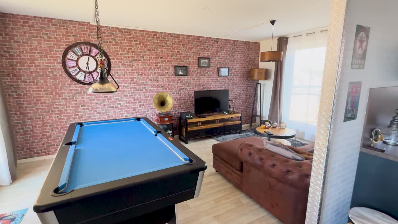 Camera slowly pans across a vintage-inspired lounge room with a blue pool table, brick accent wall, antique decor, and warm natural lighting