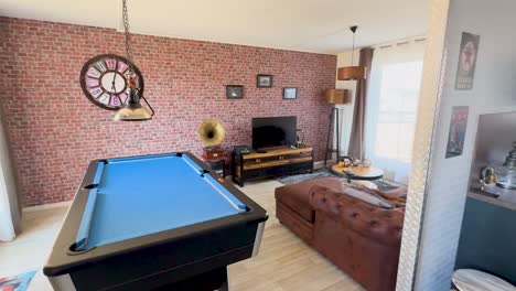 camera slowly pans across a vintage-inspired lounge room with a blue pool table, brick accent wall, antique decor, and warm natural lighting
