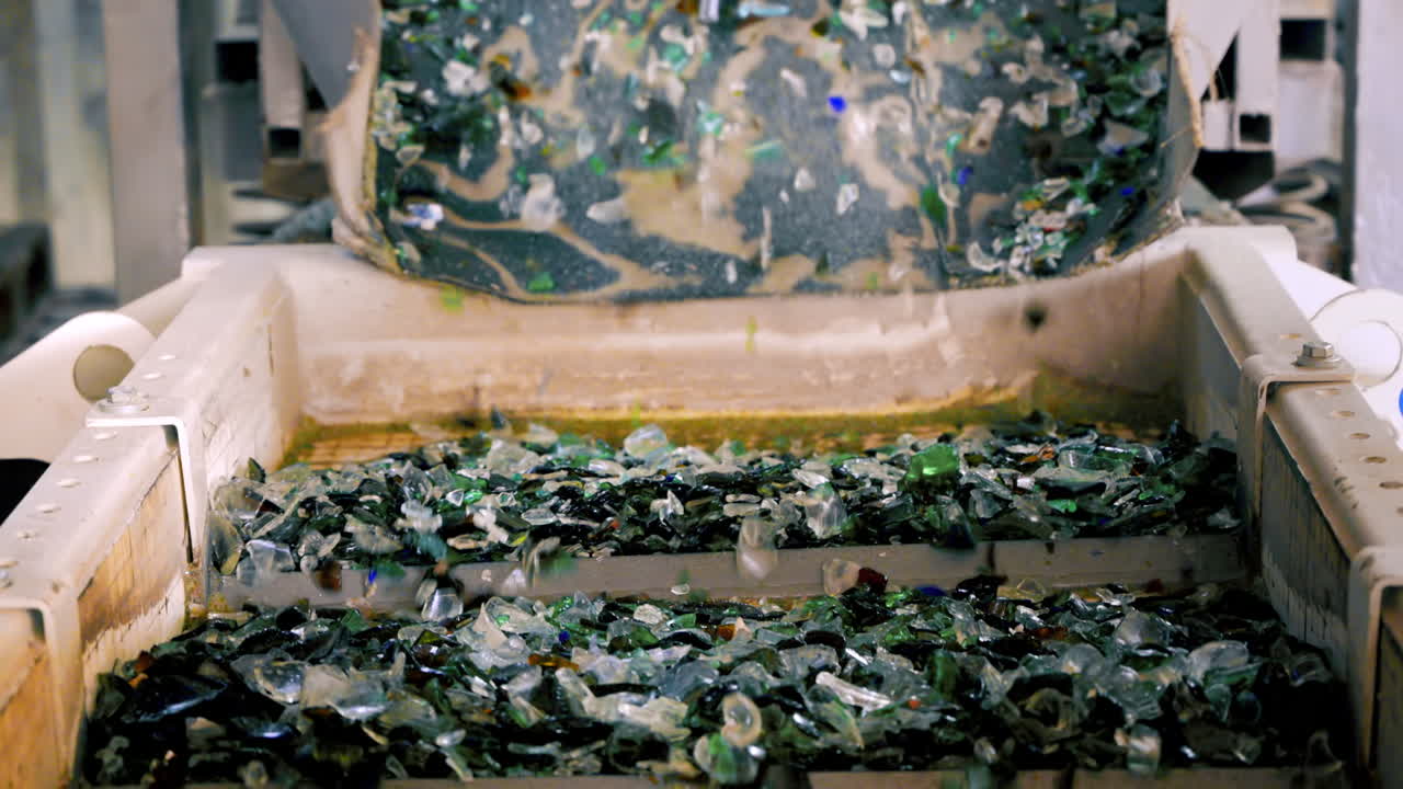 Worker in special gloves sorting glass garbage on a vibrating conveyor belt at waste sorting plant