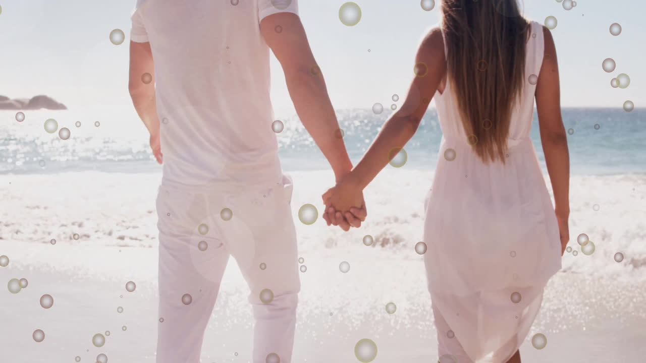 Couple holding hands walking on beach with bubbles animation overlay