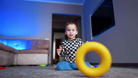 baby boy pushes the ring from pyramid to roll by the floor. happy kid playing with toys on the floor. low angle view.