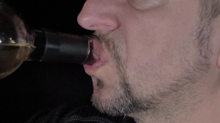 Un uomo barbuto beve vino da una bottiglia.