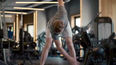 handsome strongman making hand swings at gym. sportsman warming up in sport club