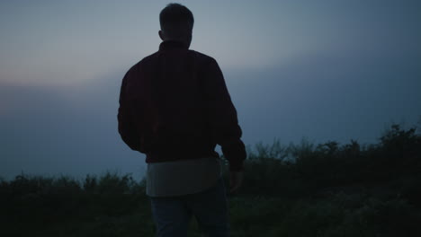 back view young guy walking in field at morning. casual man hiking in mountains