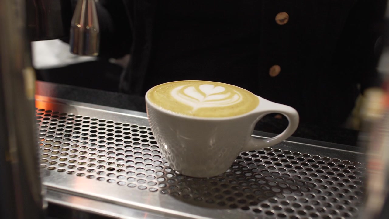 Primo piano delle mani del barista che tengono una tazza di caffè latte bianca con elegante latte art a tulipano in un caffè professionale
