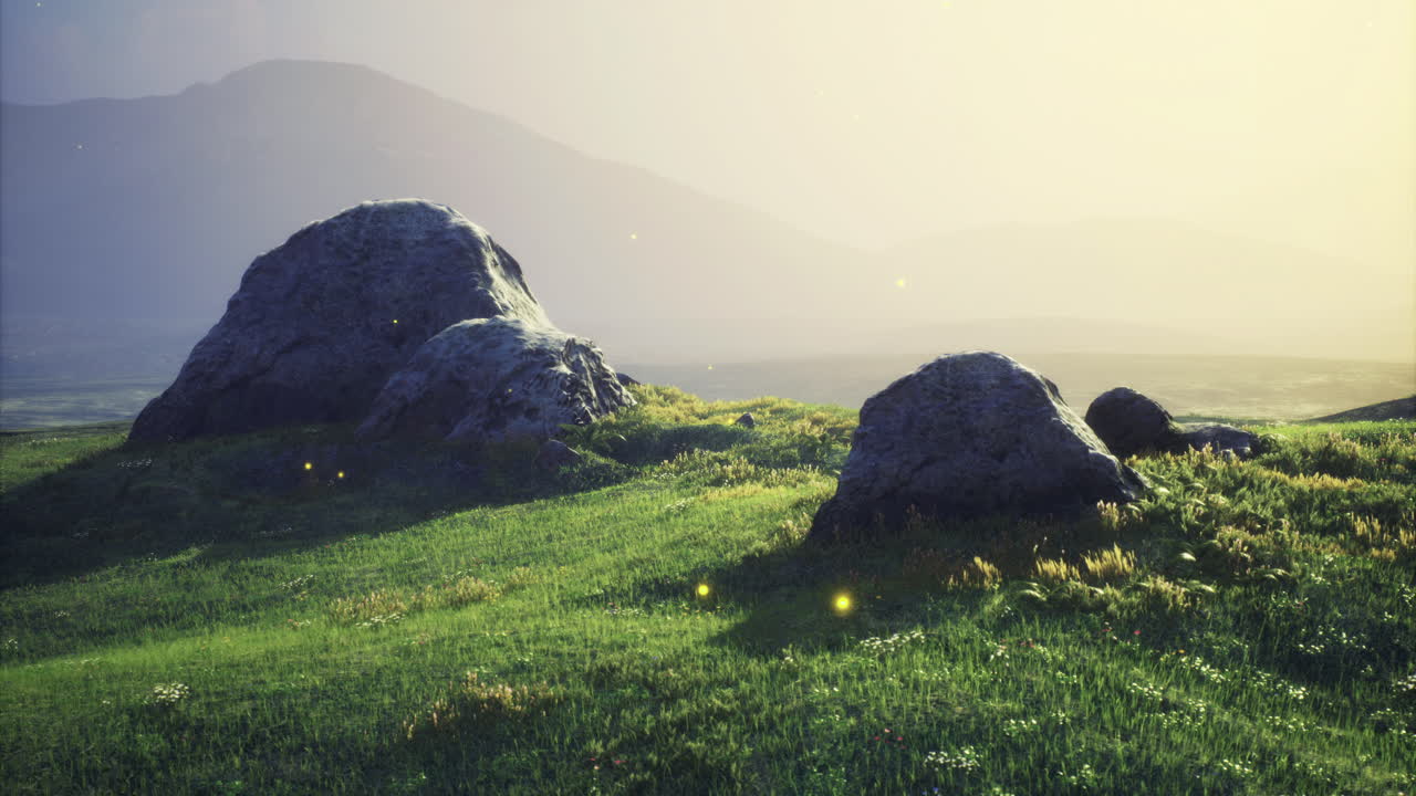 Boulders on a serene grassy field during golden hour with distant mountains