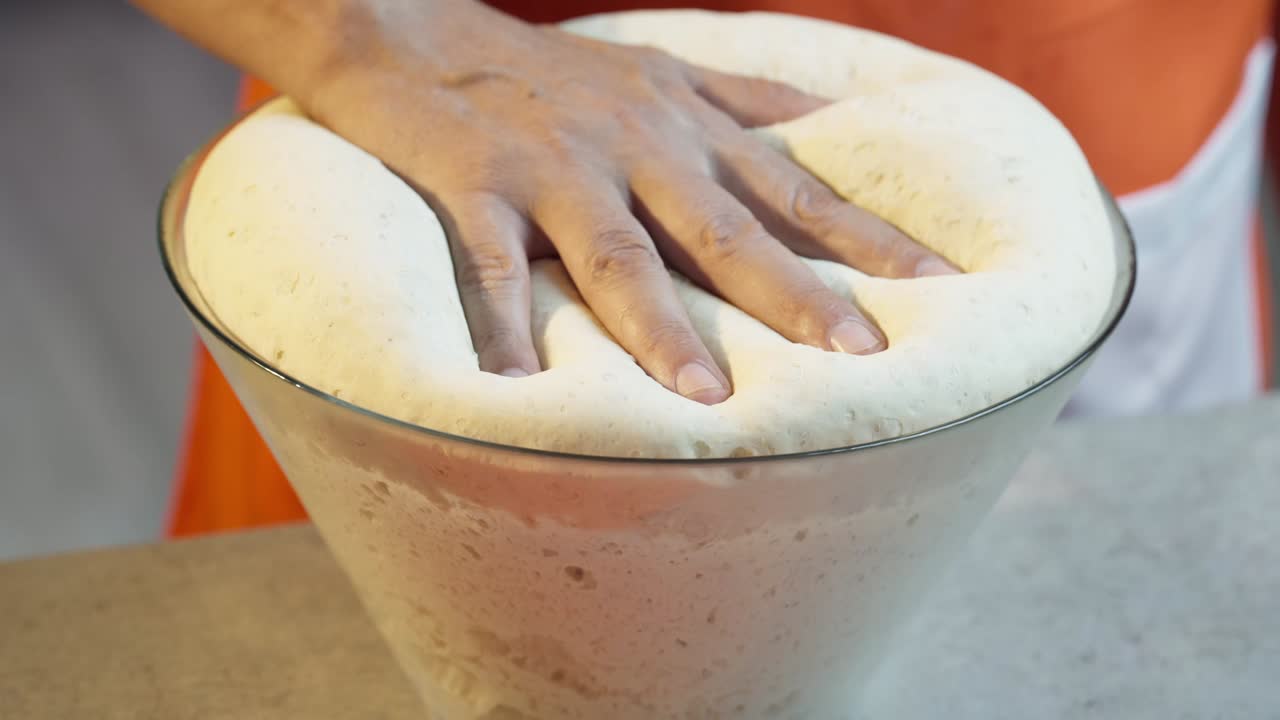 Close-up of a hand pressing soft, risen dough in a glass bowl. Perfect for ASMR, food videos, baking tutorials, or artisan bread-making visuals