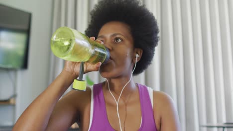 happy african american wearing sportswear, using smartphone, drinking water