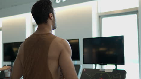 Rear-View-of-Active-Man-in-30th-Walking-on-Treadmill-and-Stretching-Hands-Wrists