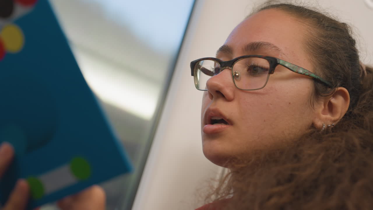 Une dame lit à voix haute. Une passagère récite doucement dans le train. Une voyageuse concentrée raconte pendant le trajet en train. Une femme aux cheveux bouclés se concentre et récite des mots tranquillement dans un train en mouvement.