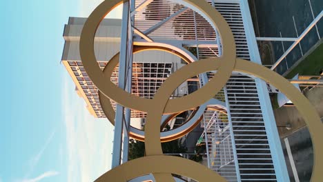 Vertical-panning-shot-of-golden-Olympic-rings-on-bridge-in-Atlanta-City-at-golden-sunset