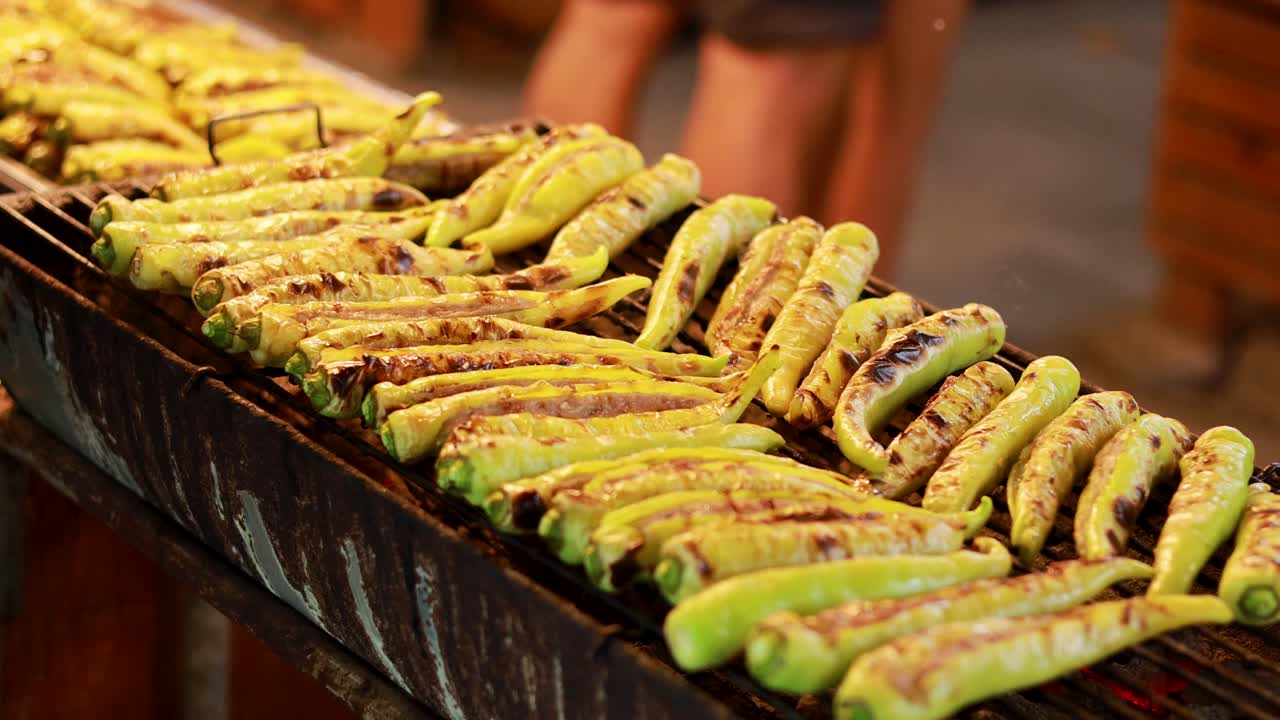 Chilies grilling over open flame at Khlong Lat Mayom Floating Market. Warm lighting highlights vibrant colors and bustling market atmosphere
