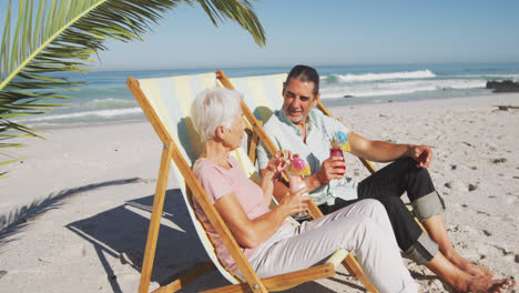 senior caucasian couple sitting on sunbeds at the beach.