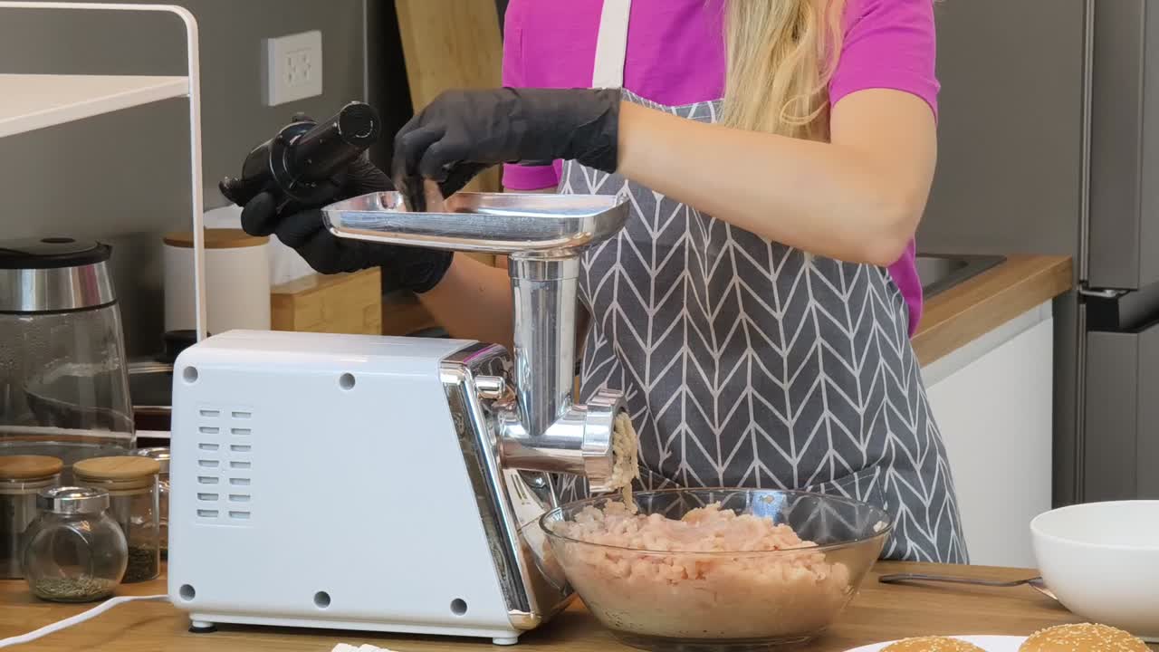 mujer usando un molinillo de carne para preparar pollo molido para hamburguesas
