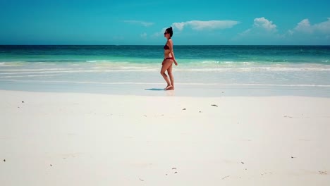 female tourist in bikini walking on pristine white sand beach in kilifi, kenya on a sunny summer day