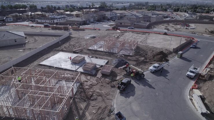 A drone elegantly circles a telehandler, poised and awaiting instructions on a bustling home construction site, capturing the precision and readiness of construction equipment in action