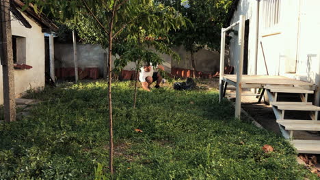 motion time lapse a skillful young man weeding grass and gathering it in a bag in the backyard of a house during a sunny day