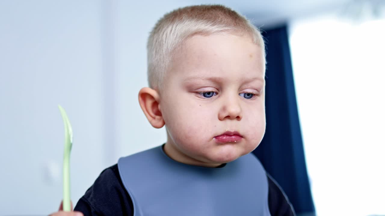 Child enjoys meal at home while wearing a bib and holding a piece of food in hand during the afternoon