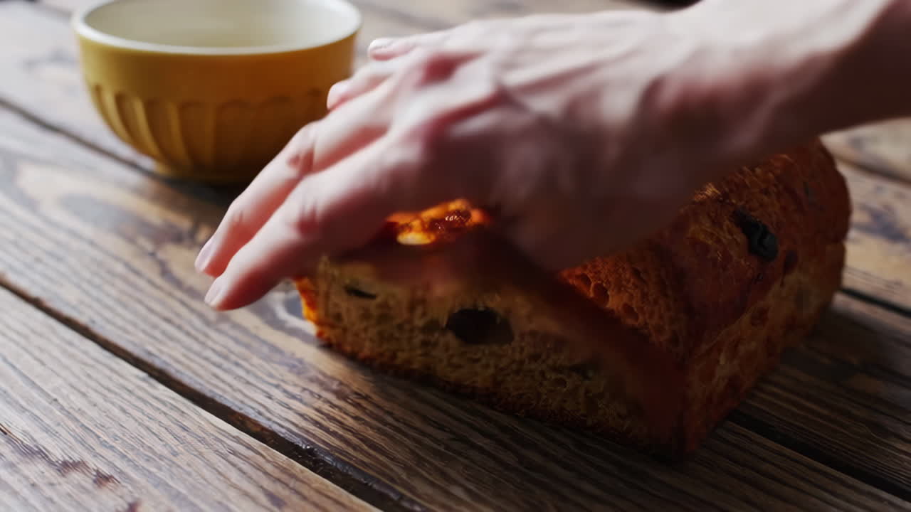 A person's hand reaching for a slice of raisin bread with butter on a wooden table