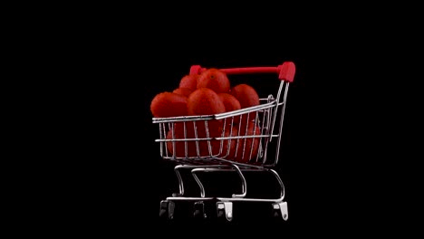 carrito de compras con tomates de uva roja montado con gotas de agua. girando en la mesa giratoria. aislado en el fondo negro. primer plano. macro.