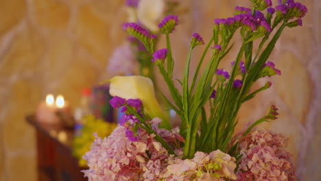 a dynamic pan shot captures a soothing, relaxing environment with a colorful bouquet of blooming flowers sets against a background of natural stone and candles with a pleasing shallow depth of field