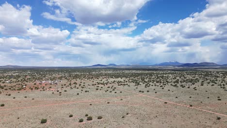 drone rising over williams, arizona, south of the grand canyon. clouds are dotting the sky over warm dirt on a bright sunny day. there are dirt roads, mountains and a few structures. rain in the back