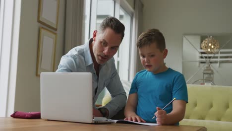 Caucasian-father-with-son-sitting-at-table-and-learning-with-laptop-at-home