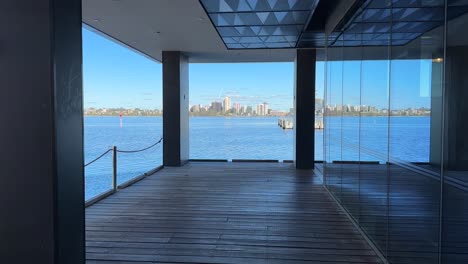 Looking-down-corridor-of-blue-with-reflections-in-full-length-glass-windows-on-boardwalk-dock-to-the-blue-water-of-the-Swan-River,-Perth,-Western-Australia