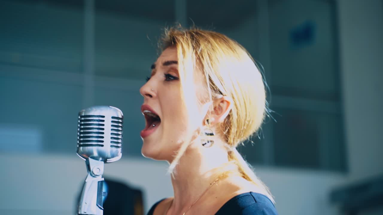Side view of young professional female singer. Face of a beautiful girl performing song on stage into the microphone. Musical concert.