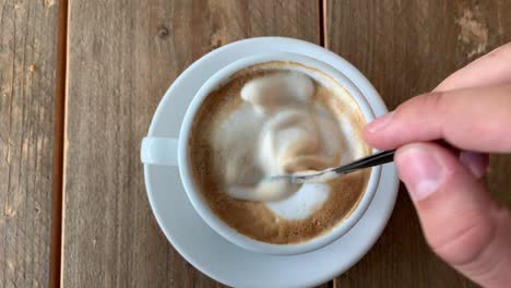 above-view-of-coffee-being-stirred-with-a-spoon,-mans-hand