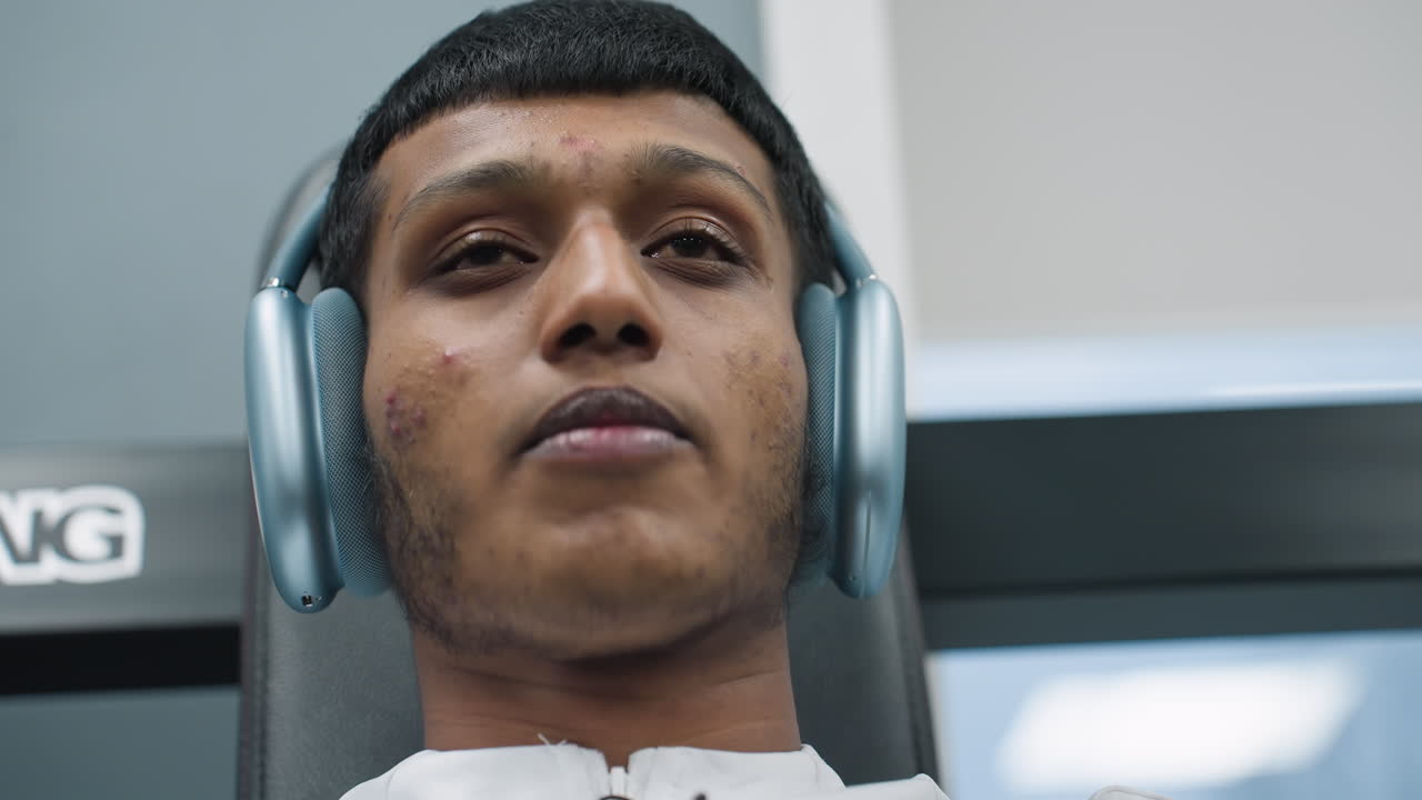 close up focused gym enthusiast adjusting over ear headphones while resting back against fitness bench preparing to lift weights with intense concentration and calm breathing