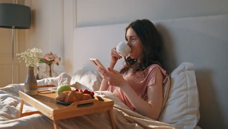 home girl enjoying morning coffee on weekend. relaxed woman holding smartphone