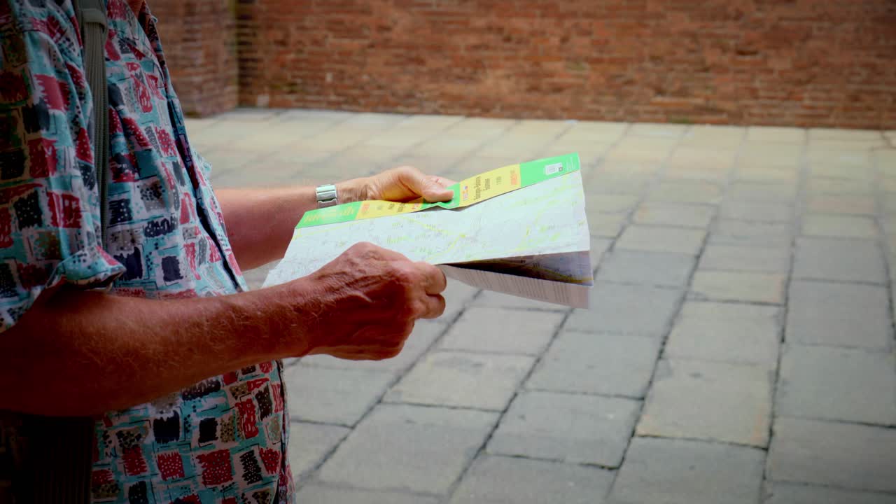 Mani che tengono una mappa di carta piegata mentre si è in piedi su un pavimento di pietra sotto i portici di Bologna