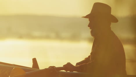 Close-up-view-of-senior-caucasian-man-floating-with-oars-in-a-boat-in-the-dawn-in-the-middle-of-the-lake