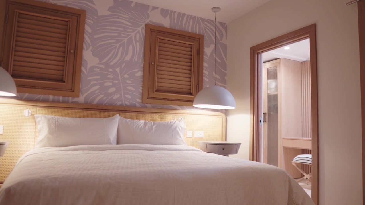 Movimento fluido della telecamera in avanti che mostra una moderna suite d'hotel a Saint Vincent e Grenadine. L'inquadratura passa dalla camera da letto principale con arredamento tropicale alla cabina armadio integrata.