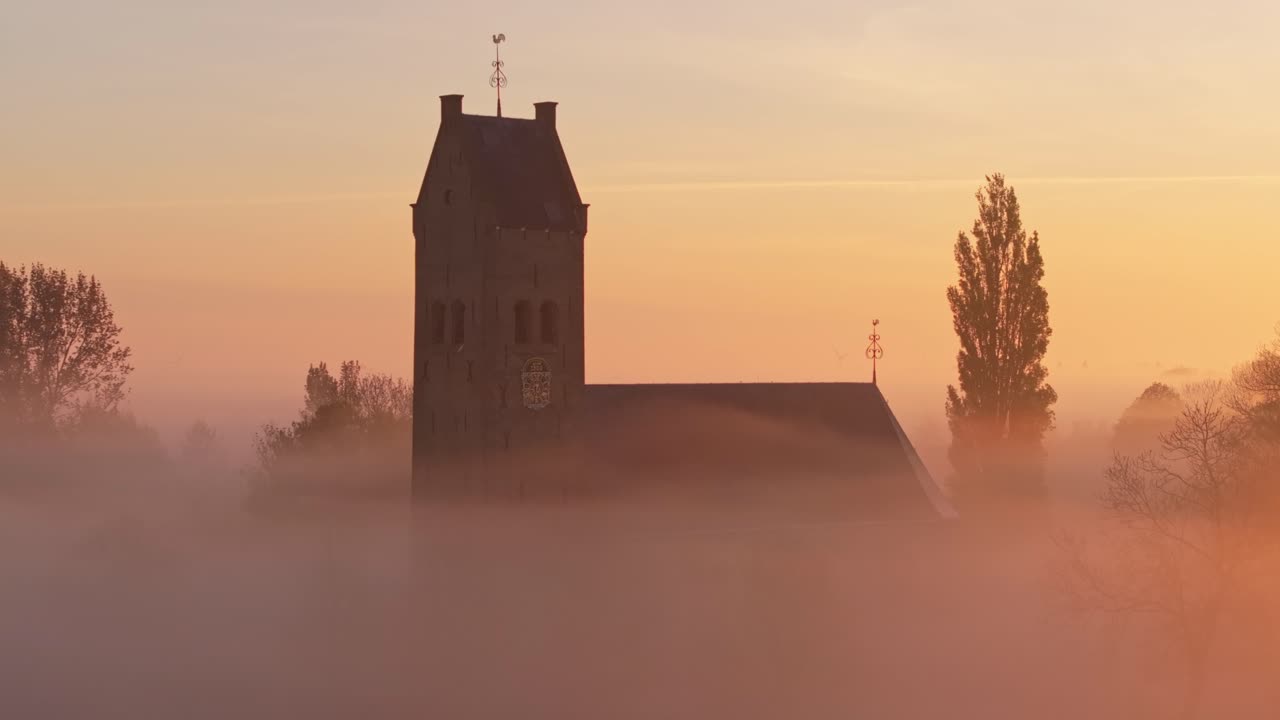 Luftfoto af landsbykirke i Friesland ved vandet i morgendis