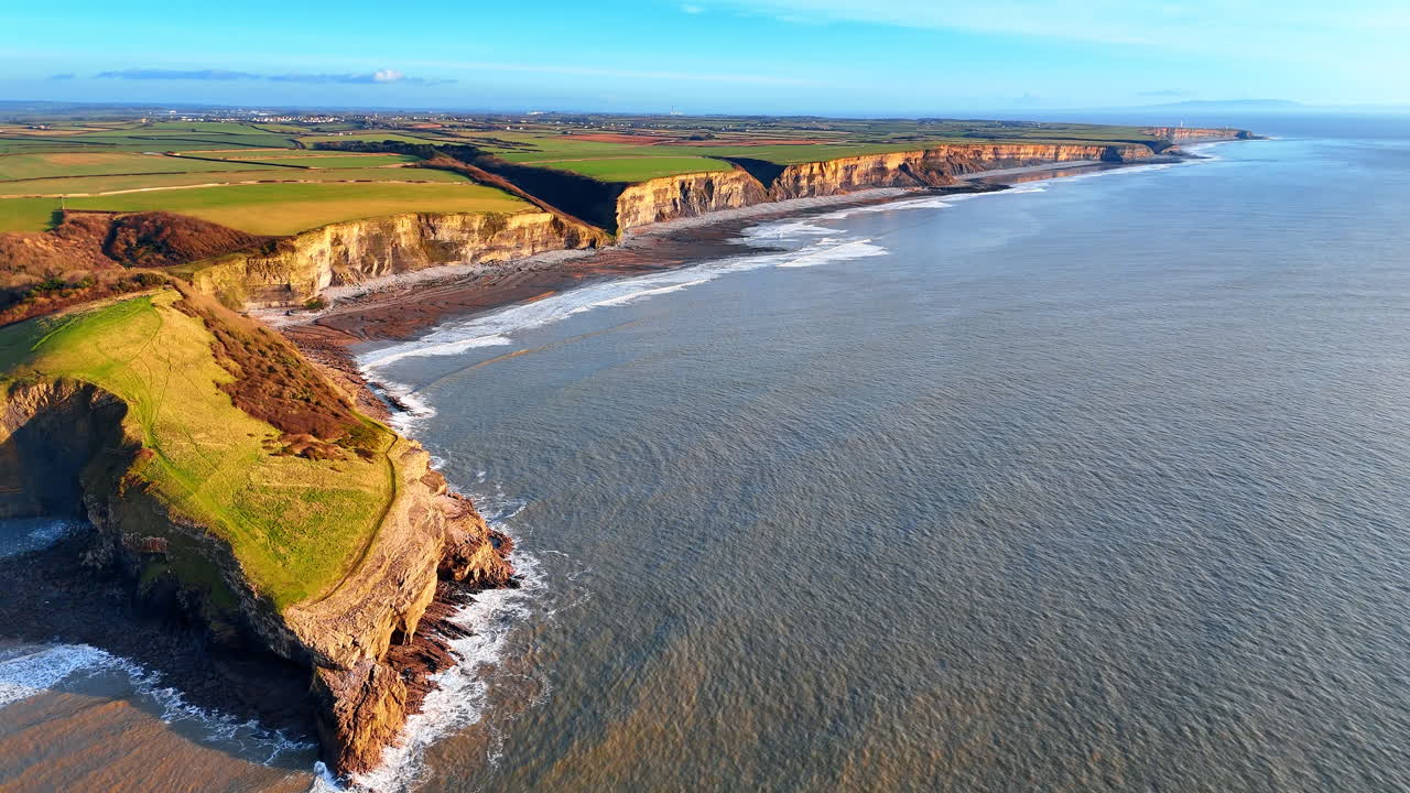 Vista aerea di scogliere costiere e costa con campi verdi. Paesaggio costiero con ripide scogliere rocciose a picco sull'oceano e campi agricoli verdi sovrastanti in Galles