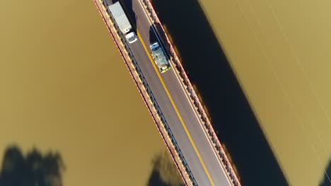 Drohnenaufnahmen-Beim-Aufsteigen-Und-Schwenken-über-Eine-Brücke,-Die-Einen-Braunen-Fluss-überspannt,-Mit-Vorbeifahrenden-Autos