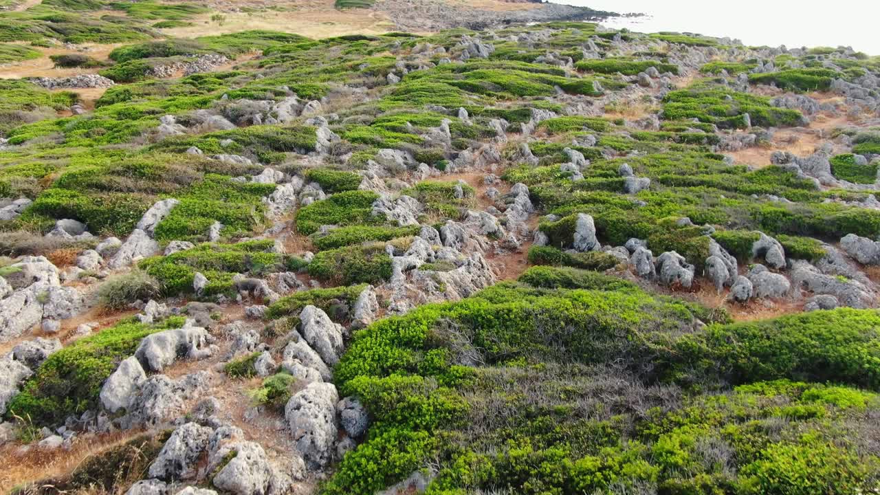Aerial flight above rocks, green patches of grass alongside coastline, Crete, Greece