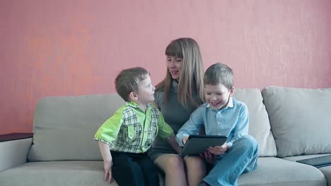 mother and two little toddler sons sit on sofa playing on tablet