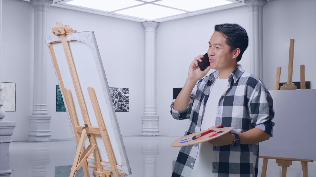 갤러리에서 오일 페인트와 브러쉬로 캔버스에 그림을 그리는 동안 스마트폰으로 이야기하는 아시아 남성 예술가