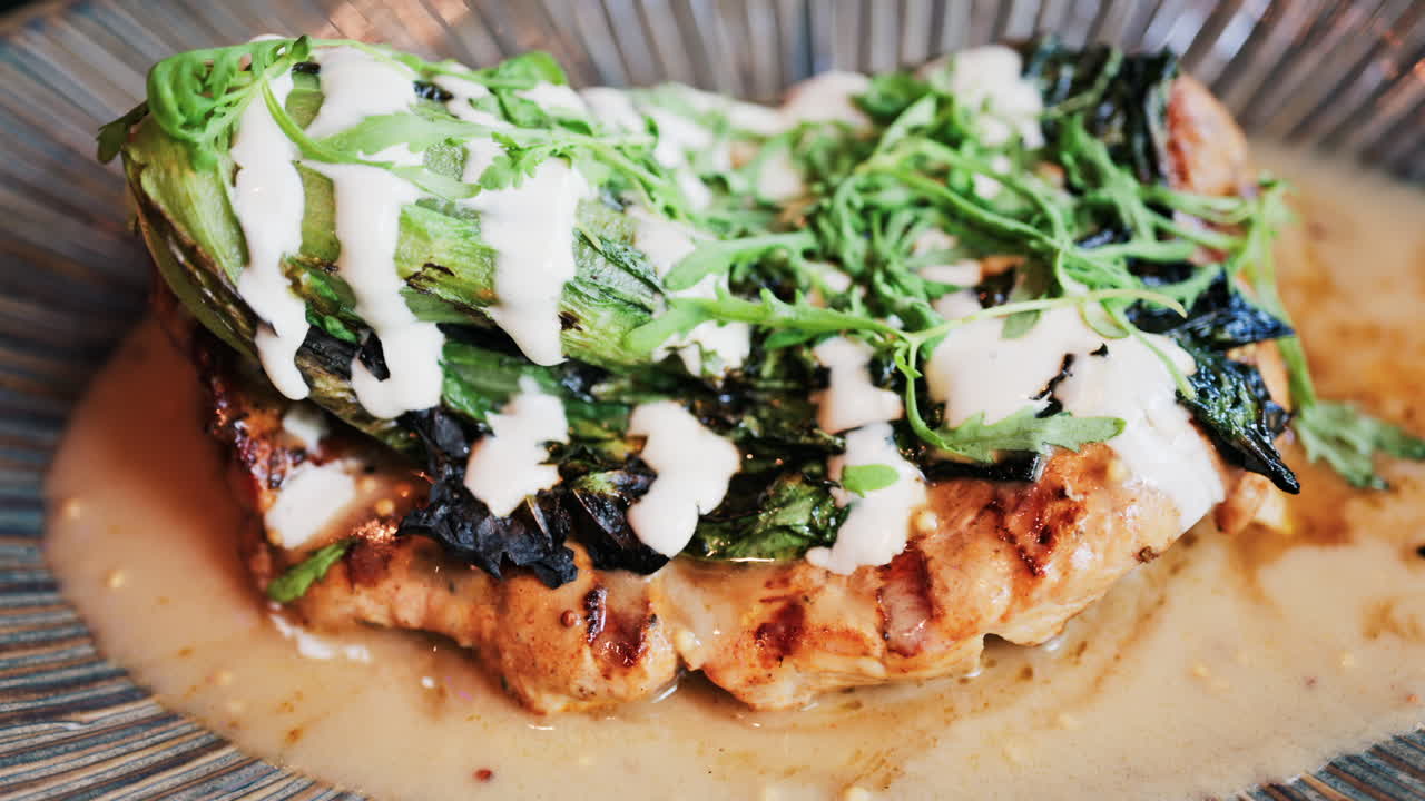 Close up of a grilled chicken breast with charred greens and a creamy dressing on a plate