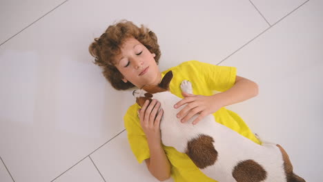 top view of a blond boy with curly hair lying on the floor and caresses his dog 1