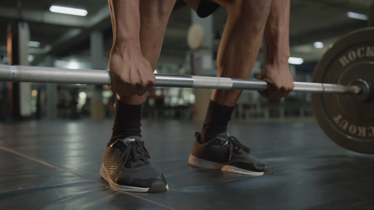 Close-up view of man's feet and hands holding a barbell