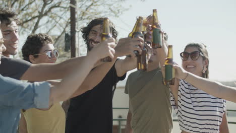 amigos felices tintineando botellas de cerveza mientras hacen una fiesta en la azotea