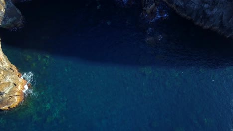 Drone-ascent-revealing-coastal-rocky-cliffs-with-crystal-sea-water-below-in-volcanic-Sao-Miguel-island,-Azores