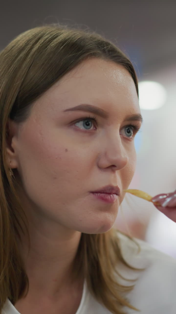 primer plano de una dama comiendo papas fritas con una mirada seria, luces parpadeantes coloridas suavemente borrosas en el fondo de un animado centro comercial, capturado en un entorno animado de un centro comercial