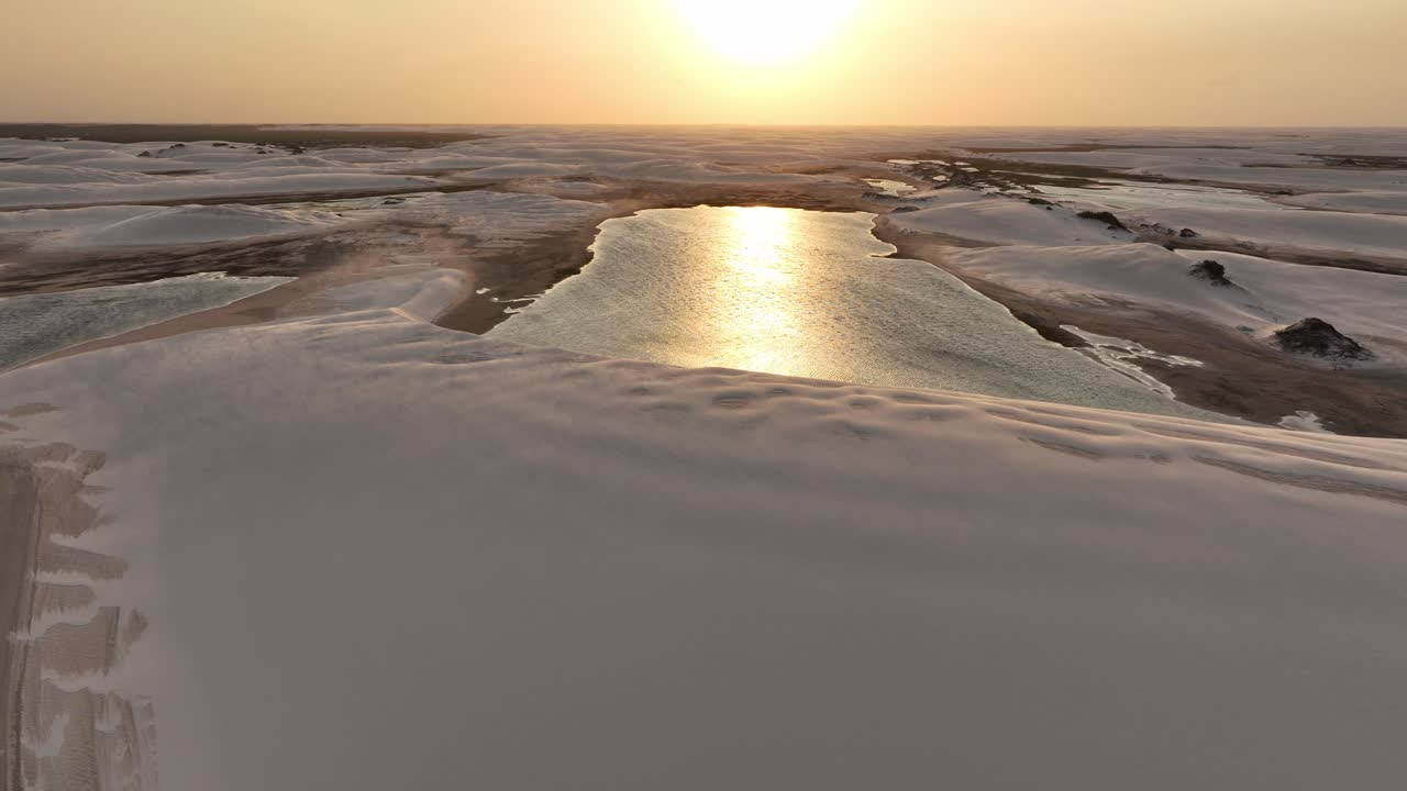 Sunset over the reflective lagoons of Lencois Maranhenses, Brazil, casting a golden glow on the dunes, aerial panoramic overview