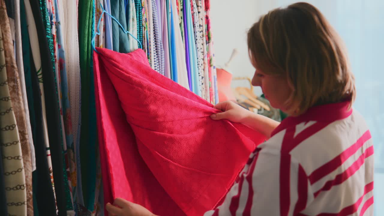 Una donna esamina un tessuto rosso tra tessuti colorati. Si concentra attentamente, selezionando il materiale per lavori artigianali o di cucito. Perfetto per progetti di moda, vendita al dettaglio o design.